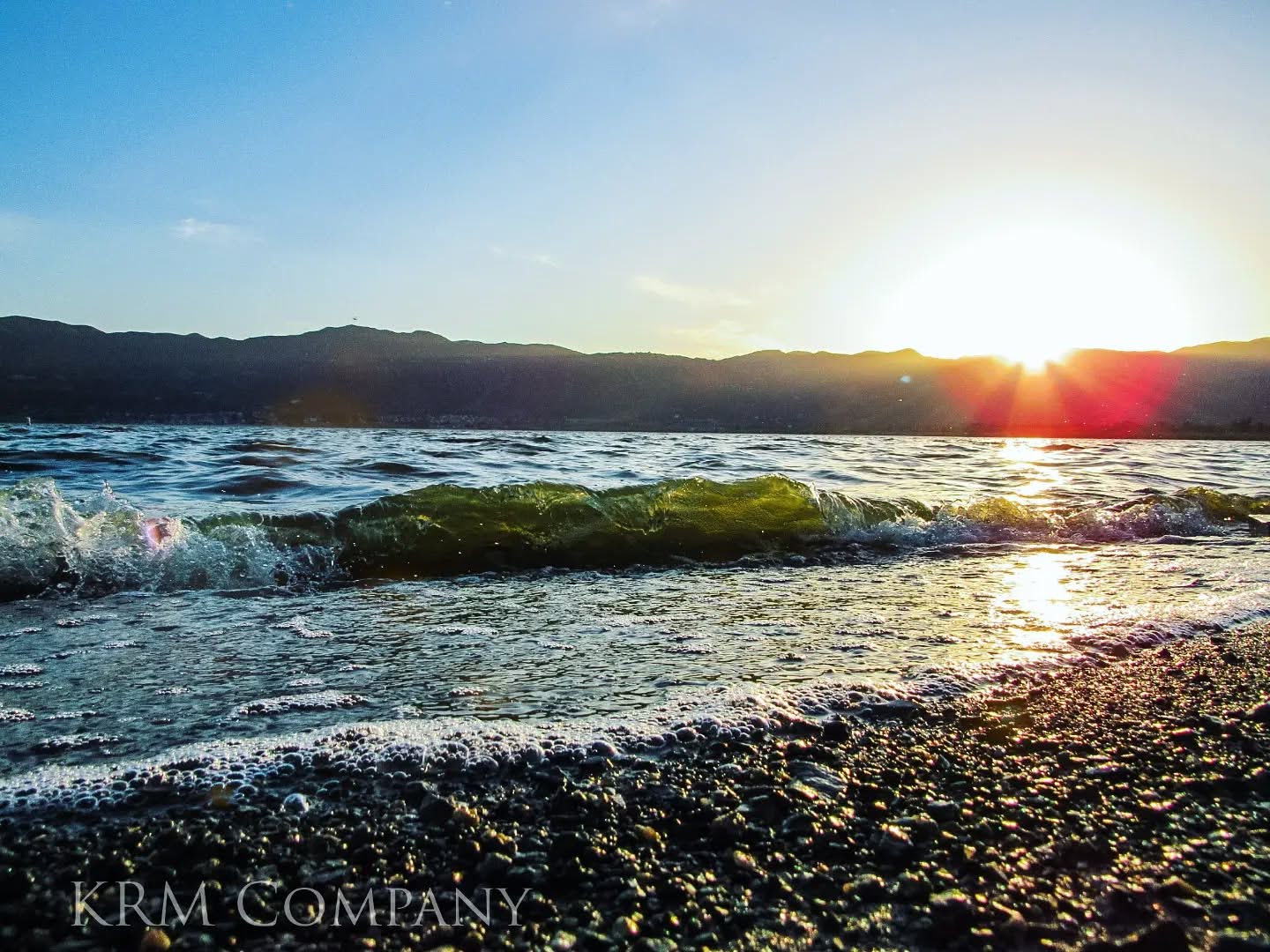 Sunset breaking over a mountain ridge above a cresting lake wave